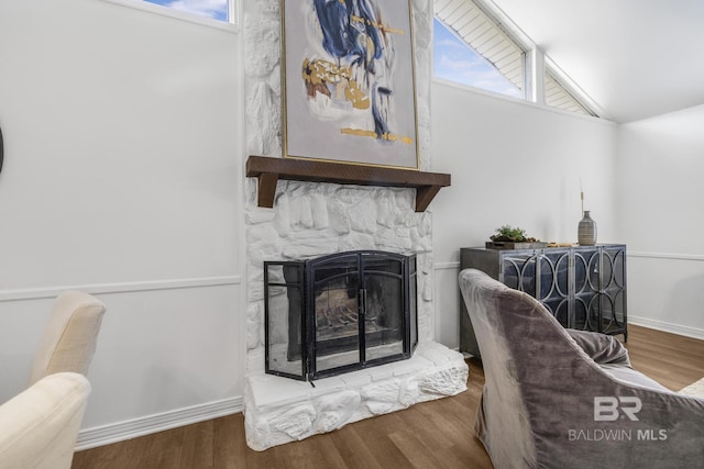 living area featuring baseboards, lofted ceiling, wood finished floors, and a fireplace