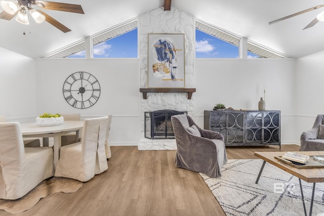 living area featuring vaulted ceiling with beams, baseboards, ceiling fan, a stone fireplace, and wood finished floors