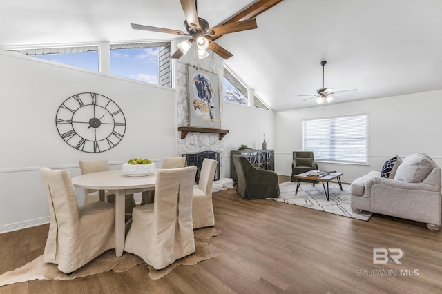 dining area featuring a stone fireplace, high vaulted ceiling, wood finished floors, and ceiling fan