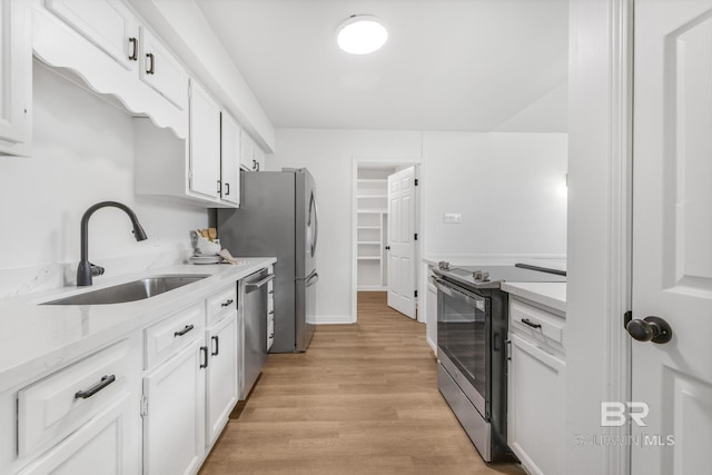 kitchen with a sink, light stone counters, light wood-style floors, appliances with stainless steel finishes, and white cabinets