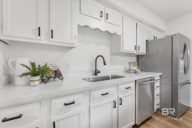 kitchen with a sink, light stone counters, white cabinetry, appliances with stainless steel finishes, and light wood finished floors