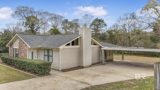 view of property exterior featuring a carport, concrete driveway, roof with shingles, and a chimney