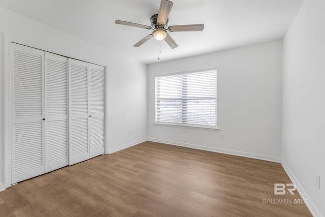 unfurnished bedroom with ceiling fan, wood finished floors, a closet, and baseboards