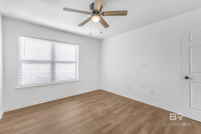 spare room with wood finished floors, a ceiling fan, and baseboards