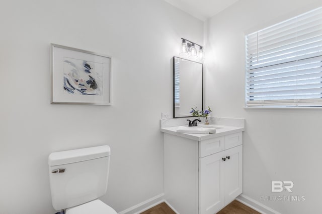 half bath featuring baseboards, toilet, and vanity