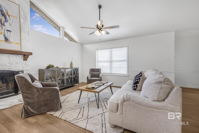 living room with wood finished floors, a ceiling fan, baseboards, a stone fireplace, and vaulted ceiling