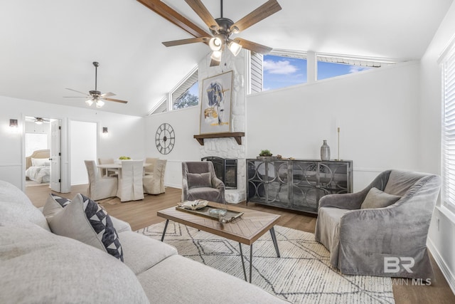 living room featuring a stone fireplace, wood finished floors, a ceiling fan, and high vaulted ceiling