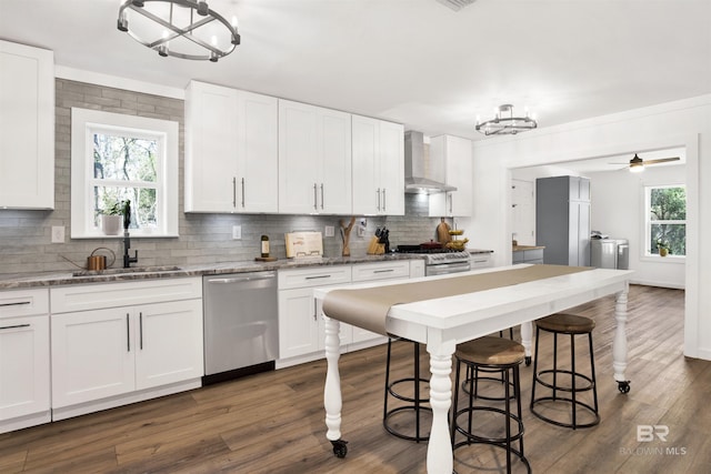 kitchen with decorative backsplash, appliances with stainless steel finishes, washer and dryer, wall chimney range hood, and a sink