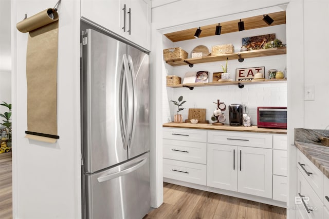 interior space with freestanding refrigerator, white cabinetry, backsplash, and light wood finished floors