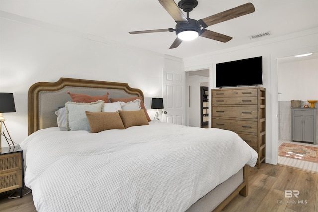 bedroom featuring ceiling fan, wood finished floors, visible vents, and crown molding