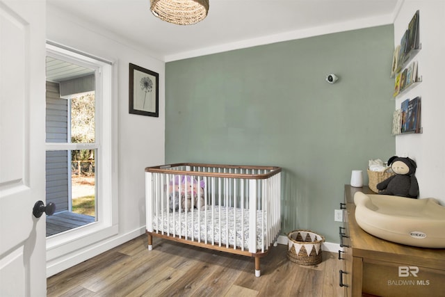 bedroom featuring a nursery area, crown molding, baseboards, and wood finished floors