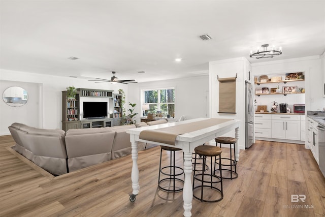 kitchen with visible vents, white cabinets, light wood-type flooring, stainless steel fridge, and ceiling fan with notable chandelier