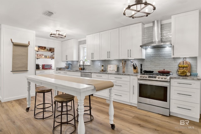 kitchen featuring visible vents, an inviting chandelier, appliances with stainless steel finishes, white cabinets, and wall chimney exhaust hood