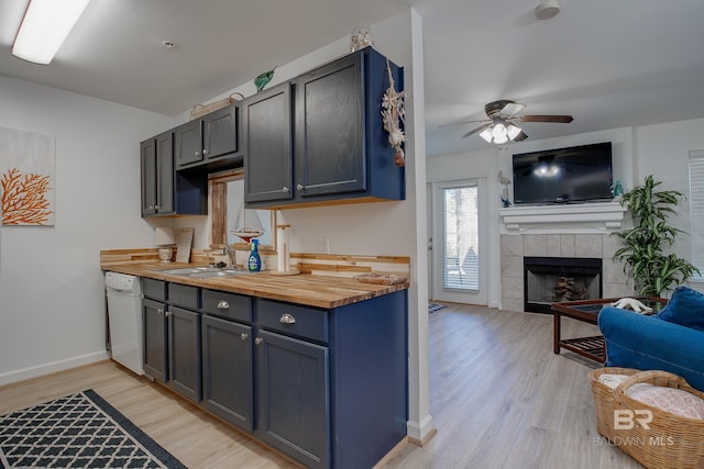 kitchen featuring a sink, a fireplace, light wood finished floors, wooden counters, and dishwasher