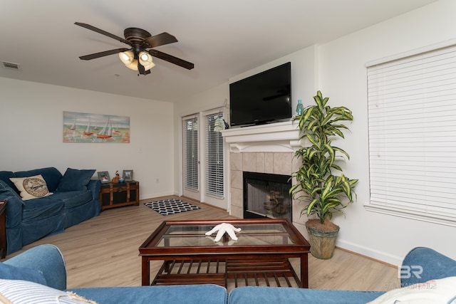 living room with a tiled fireplace, wood finished floors, visible vents, and baseboards