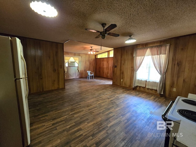unfurnished living room with a textured ceiling, ceiling fan, baseboards, wood walls, and dark wood-type flooring