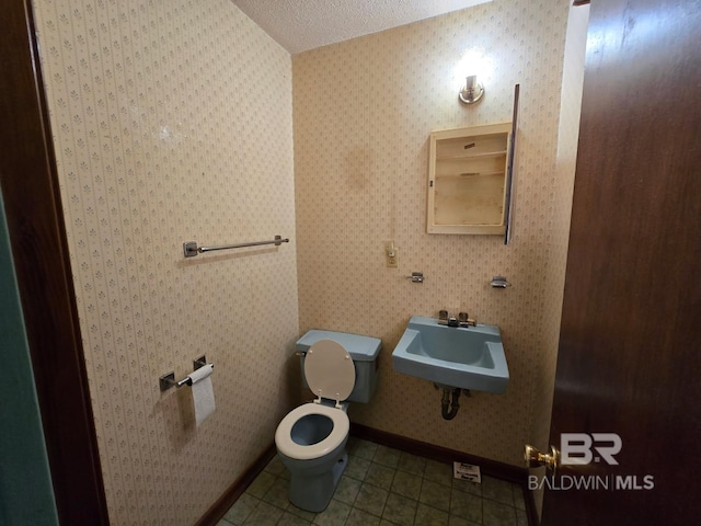 half bathroom with tile patterned floors, toilet, a sink, baseboards, and a textured ceiling