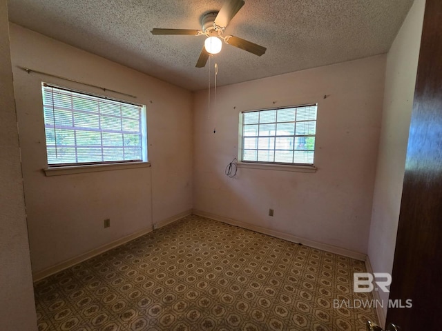empty room featuring a textured ceiling, baseboards, ceiling fan, and light floors