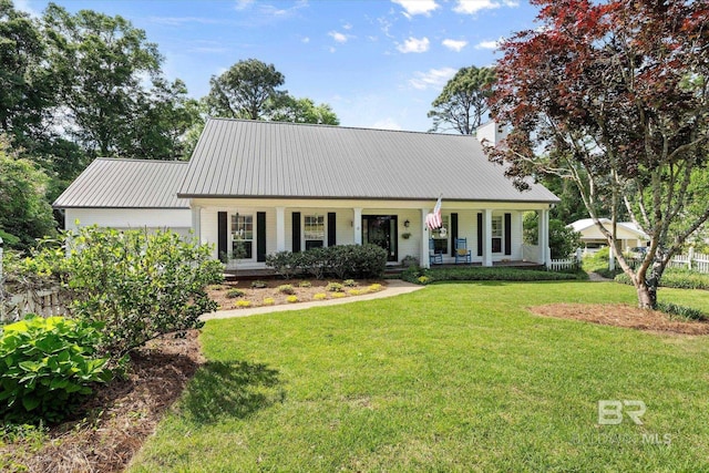 view of front of home featuring a chimney, a front yard, covered porch, and metal roof