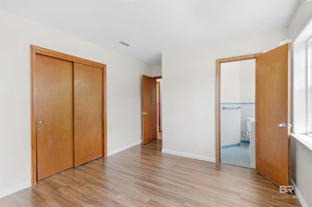unfurnished bedroom featuring ensuite bath, visible vents, light wood finished floors, and a closet