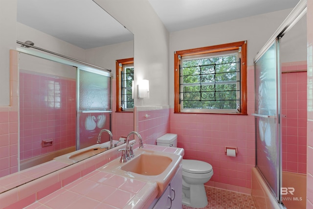 full bathroom with tile patterned floors, vanity, tile walls, bath / shower combo with glass door, and toilet