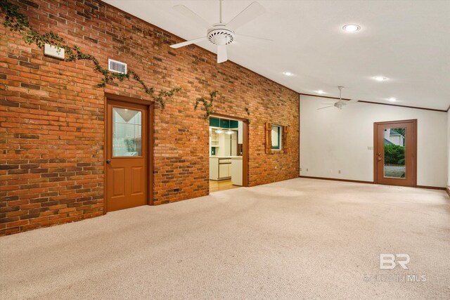 carpeted spare room with plenty of natural light, ceiling fan, vaulted ceiling, and brick wall