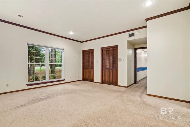 unfurnished bedroom with multiple closets, crown molding, and light colored carpet