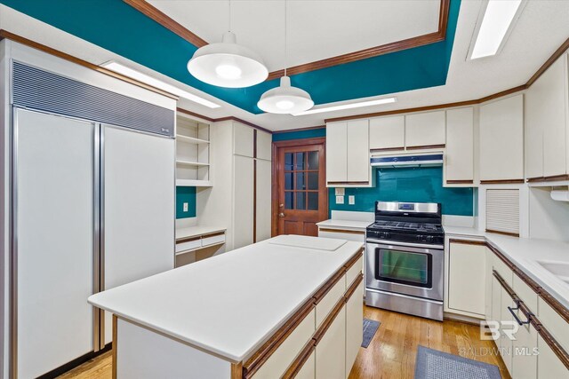 kitchen with paneled refrigerator, hanging light fixtures, gas stove, a center island, and light wood-type flooring