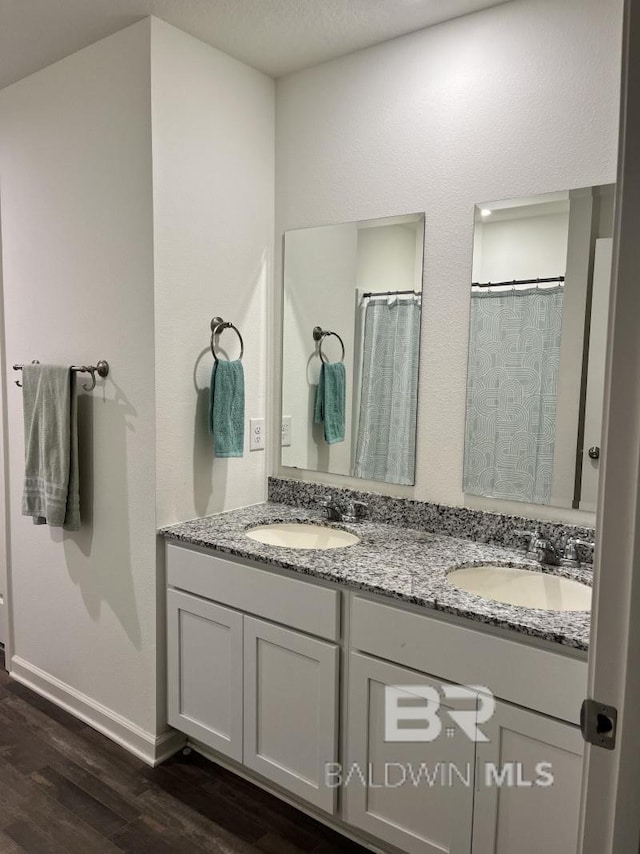 bathroom featuring a sink, double vanity, baseboards, and wood finished floors
