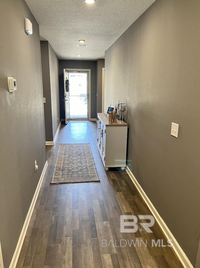 doorway with baseboards, a textured wall, a textured ceiling, and hardwood / wood-style flooring