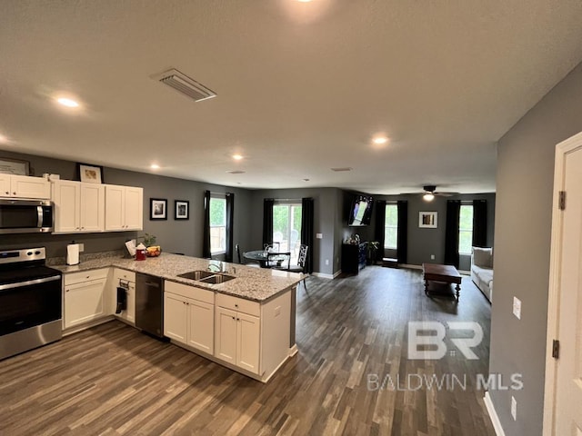 kitchen featuring visible vents, a sink, a peninsula, dark wood-type flooring, and appliances with stainless steel finishes