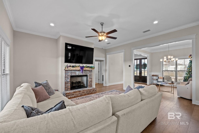 living room with crown molding, ceiling fan with notable chandelier, hardwood / wood-style floors, and a fireplace