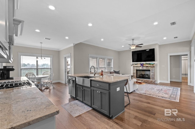 kitchen with gray cabinets, stainless steel appliances, light stone countertops, a brick fireplace, and decorative light fixtures