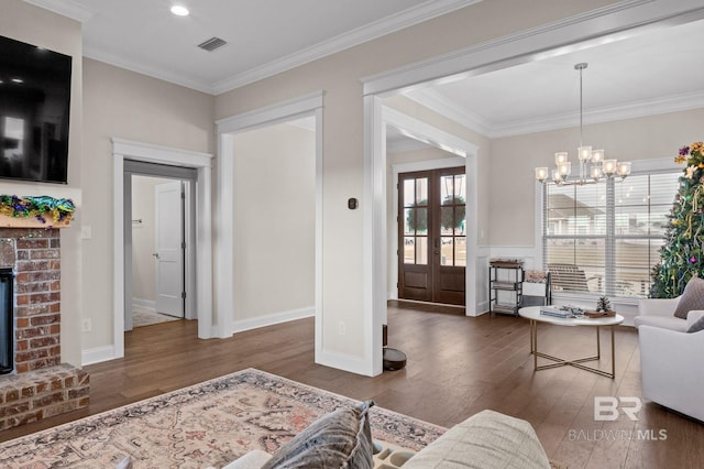 living room with ornamental molding, a brick fireplace, dark wood-type flooring, and an inviting chandelier