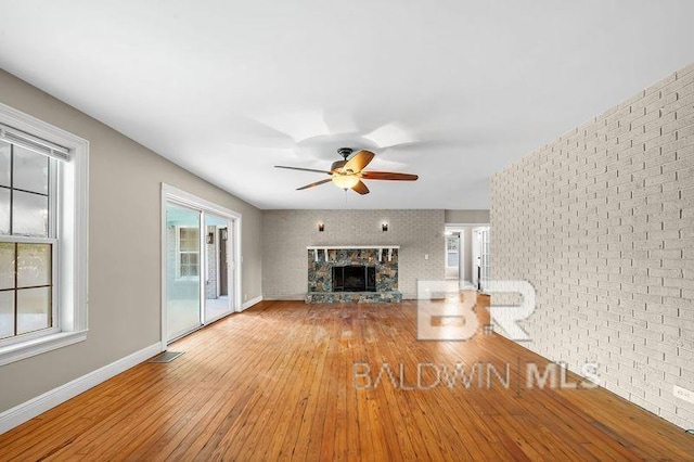 unfurnished living room with ceiling fan, light wood-type flooring, a fireplace, and brick wall