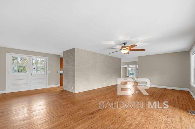 unfurnished living room featuring ceiling fan, french doors, brick wall, and light hardwood / wood-style flooring