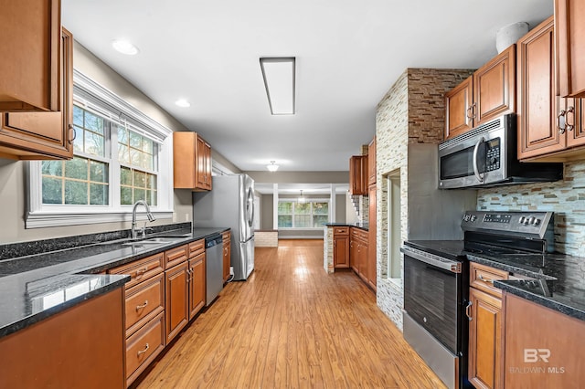 kitchen with a healthy amount of sunlight, dark stone countertops, light wood-type flooring, and appliances with stainless steel finishes