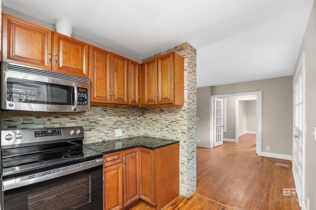 kitchen with decorative backsplash, light hardwood / wood-style floors, dark stone countertops, and appliances with stainless steel finishes