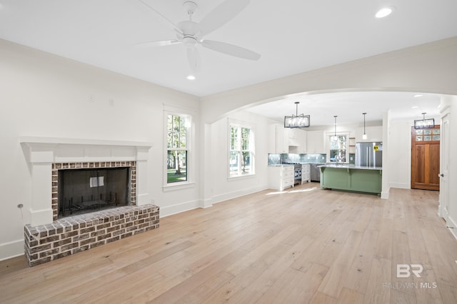 unfurnished living room with a brick fireplace, ceiling fan, and light hardwood / wood-style flooring