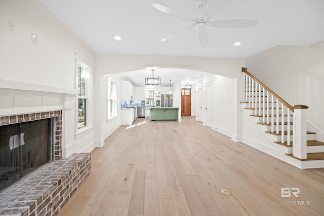 unfurnished living room with a fireplace, light wood-type flooring, and ceiling fan