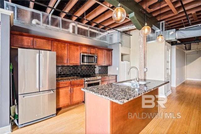 kitchen with sink, light hardwood / wood-style flooring, hanging light fixtures, dark stone counters, and stainless steel appliances