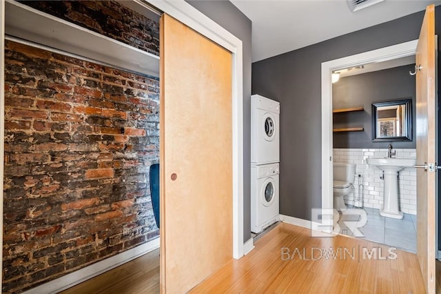 clothes washing area featuring hardwood / wood-style flooring, stacked washing maching and dryer, tile walls, a baseboard heating unit, and brick wall