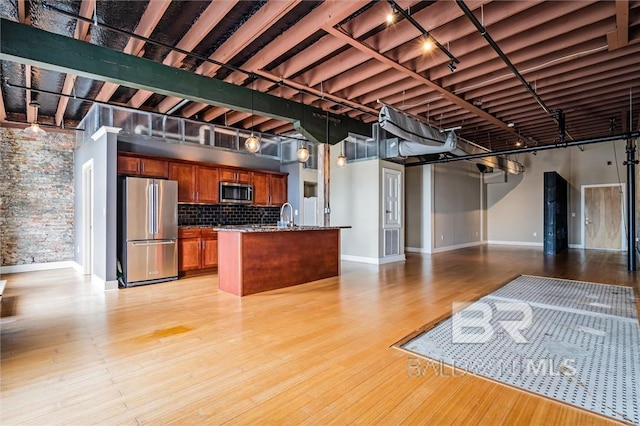 kitchen with appliances with stainless steel finishes, tasteful backsplash, a center island with sink, dark stone counters, and light wood-type flooring