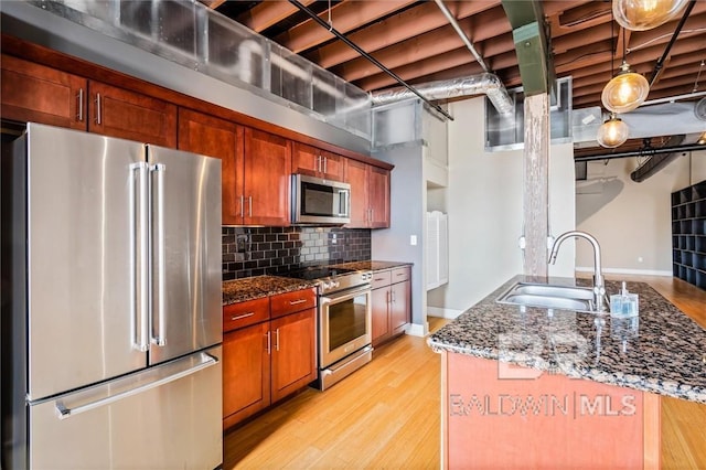 kitchen featuring tasteful backsplash, sink, dark stone countertops, stainless steel appliances, and light wood-type flooring