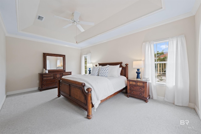 bedroom with a tray ceiling, light colored carpet, visible vents, and ornamental molding