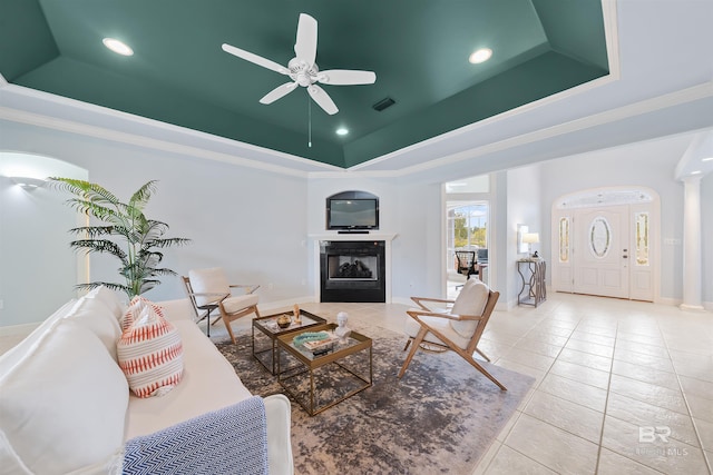 tiled living area featuring visible vents, crown molding, decorative columns, a fireplace, and a raised ceiling