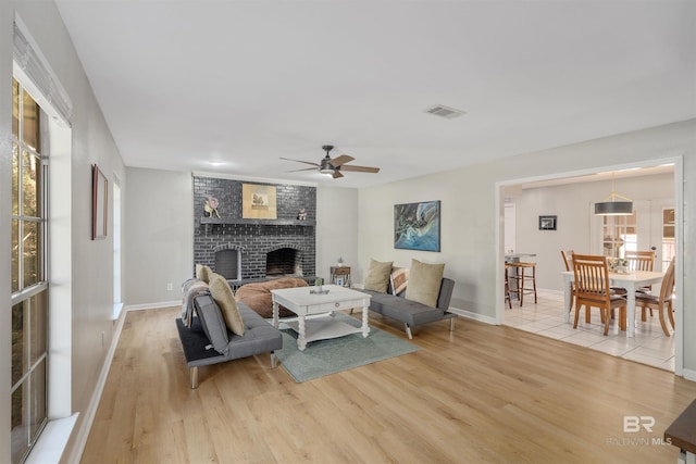 living room with a brick fireplace, ceiling fan, and light wood-type flooring