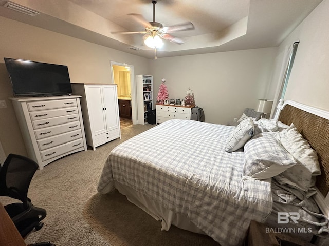 bedroom with connected bathroom, a tray ceiling, dark carpet, and ceiling fan