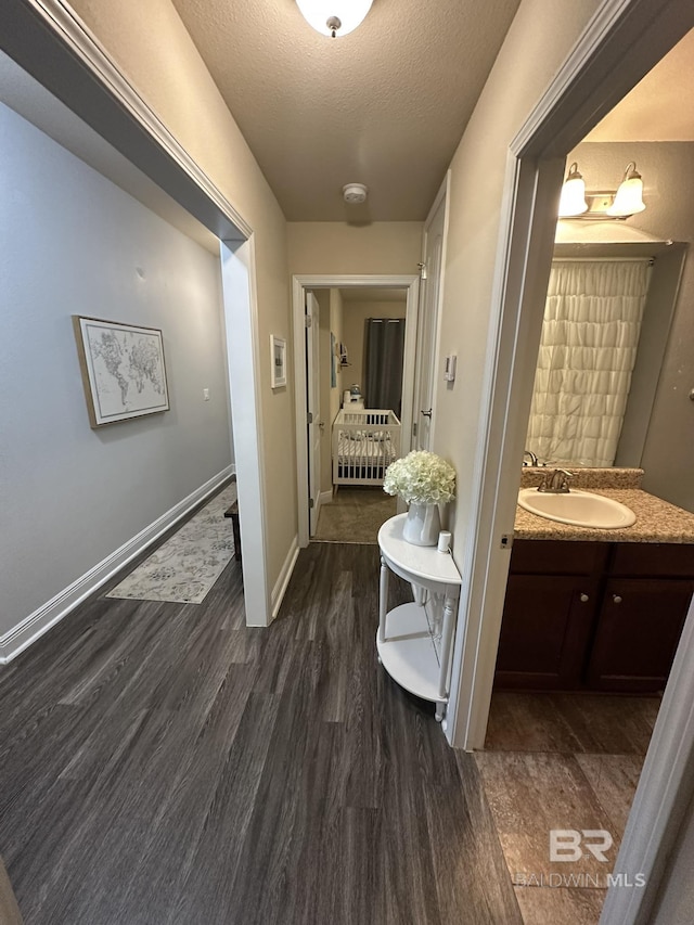 hallway with a textured ceiling, sink, and dark wood-type flooring