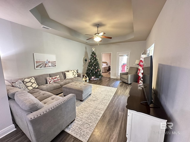 living room featuring dark hardwood / wood-style flooring, a raised ceiling, and ceiling fan